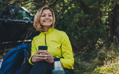 Girl smile enjoys summer nature hold hand mug of warm tea during recreation trip, happy hiker laughing showing teeth drink coffee from thermos in green forest. Happy tourist relax while traveling auto