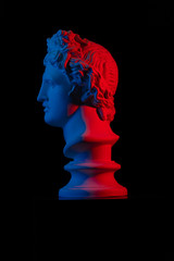 Plaster statue of a bust of Apollo Belvedere in red and blue light on a black background