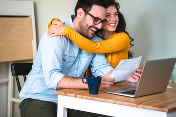 Wall Mural - Positive young couple embracing and calculating and  paying bills on laptop online at home stock photo