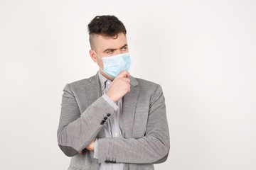 Wall Mural - Isolated portrait of stylish young European man with hand under chin and looking sideways with doubtful and skeptical expression, suspect and doubt. Standing indoors over gray background.