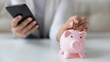© fizkes - Crop close up of woman put coin in piggy bank save money for future, use financial app on cellphone, female or housewife manage household finances or expenditures, account investment on smartphone