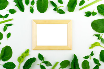 Fresh green vegetables and herbs set on a white background around an empty frame. 