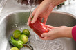 Lavando um pimentão vermelho, vista lateral de uma pessoa higienizando um legume com água na pia, para eliminar a contaminação por vírus e bactérias