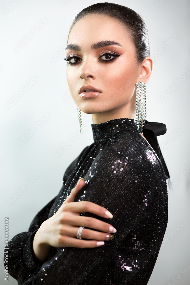 Portrait of a young beautiful elegant woman. Black sequin evening dress.  Bright makeup and smoothly combed hair. Long earrings. The hand rests on  the shoulder in the foreground. Stock-bilde | Adobe Stock
