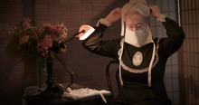 An Old Woman Sitting In Her Home Tries Out The Face Mask She Has Handmade To Wear During The 1918 Spanish Flu Pandemic.