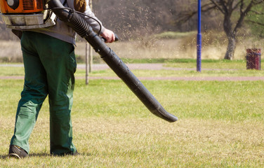 Lawn care. The gardener removes old dried grass from the lawn in the park with a gasoline portable blower.