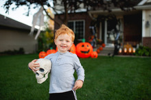 Toddler Boy Smiling While Holding Halloween Decor In Front Yard