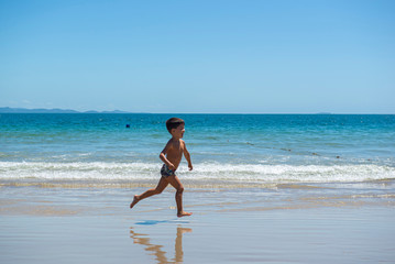 Little boy running on beach beside blue sea in a sunny day of summer.