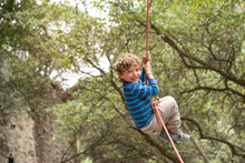 Four Year Old Toddler Smiles Hanging From A Rope With His Hands