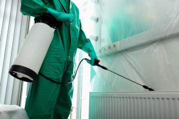 Wall Mural - Man in chemical suit getting rid of insects behind the radiator stock photo
