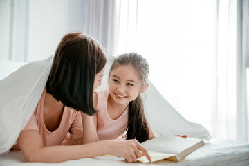 Wall Mural - happy mother and  daughter child reading book together in bed