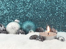 Lit Candle With Christmas Decoration On Fake Snow Against Glittering Wall
