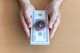 Fototapeta Konie - Man hands holding 100 dollar bills and compass on wooden table. Wealth and financial concept