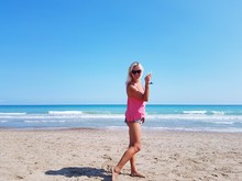 Woman Holding Wineglass Standing On Beach Against Clear Blue Sky