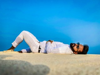 Male Model wearing white clothes and sunglasses on beach under clear blue sky