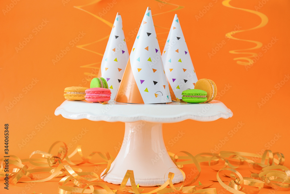 Party hats with decor and macarons on color background