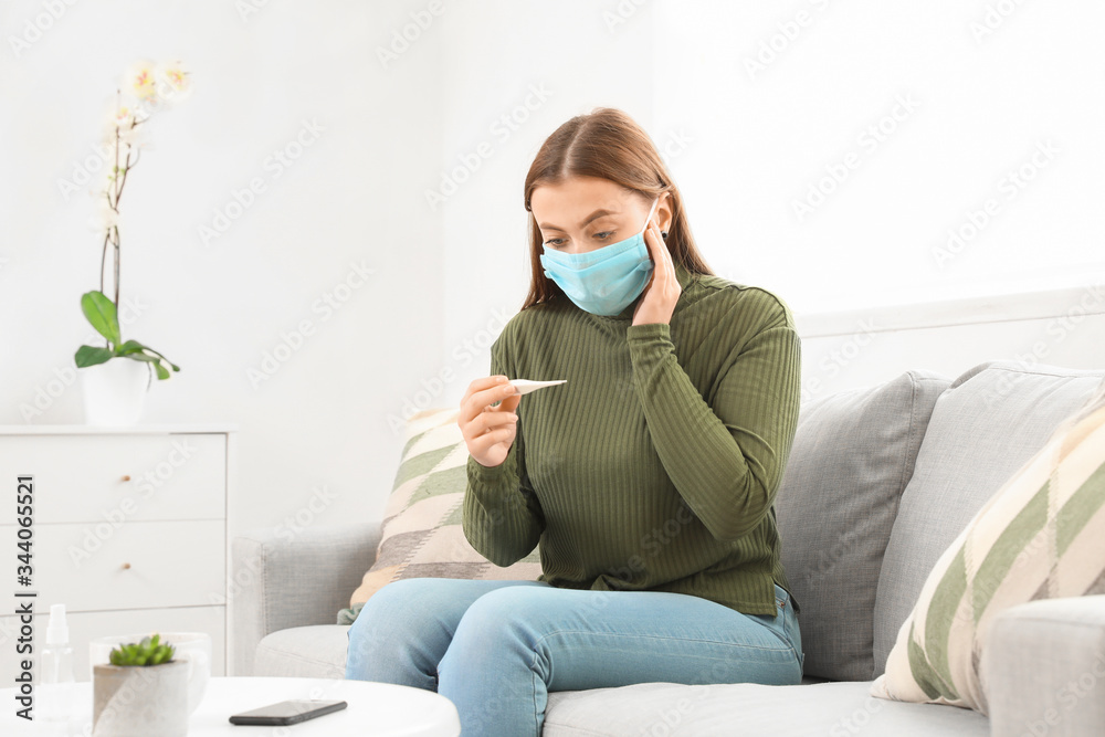 Sick woman in protective mask and with thermometer at home. Concept of epidemic