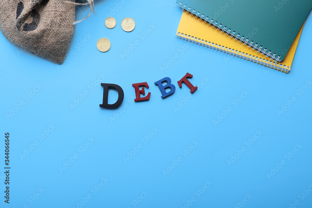 Bag with money, notebooks and word DEBT on color background