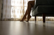 © Jantira - Woman sitting on sofa with barefoot on floor with curtain background in room.
