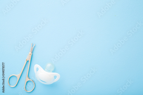Scissors and soother on light blue table. Pastel color background. Baby nail cutting. Empty place for text. Closeup. Top down view.