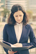 © Mangostar - Serious businesswoman reading papers. Front view of concentrated middle aged businesswoman in formal wear holding folder with documents on street. Paperwork concept