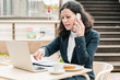 © Mangostar - Businesswoman using laptop and smartphone in cafe. Serious professional businesswoman talking by smartphone, working with papers and laptop computer while sitting in outdoor cafe. Business concept