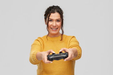 gaming, entertainment and people concept - portrait of happy smiling young woman with pierced nose with gamepad playing video game over grey background