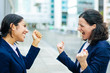 © Mangostar - Excited businesswomen celebrating success. Side view of cheerful female colleagues in formal wear raising fists at street. Winners concept
