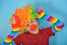 A Funny Clown Is Standing In Multi-colored Mittens And In A Wig With A Red Nose.