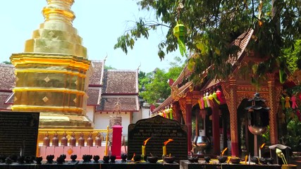 Wall Mural - CHIANG MAI, THAILAND - MAY 2, 2019: The altar with burning candles and insence sticks at the small golden chedi and ornate mondop pavilion of Wat Phra Singh temple, on May 2 in Chiang Mai