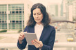 © Mangostar - Serious woman using tablet pc. Focused middle aged businesswoman using digital tablet while standing on urban city street. Wireless technology concept