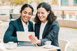 © Mangostar - Content businesswomen with tablet pc in outdoor cafe. Cheerful female colleagues sitting at table, drinking coffee and using digital tablet in outdoor cafe. Wireless technology concept