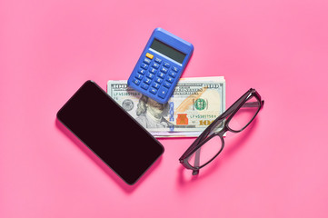 Smartphone, calculator, glasses and banknote of dollars on pink background. Concept of mobile banking. Online shopping from home. Distancing control financial balance