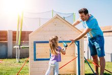 Dad And Daughter Making Assembling Wooden Playhouse At Home In Backyard Garden