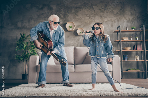 Photo of two people excited grandpa play guitar small granddaughter mic singing cool style trendy sun specs denim clothes repetition school concert stay home quarantine living room indoors