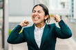 © Mangostar - Excited businesswoman celebrating success. Cheerful young businesswoman in formal wear standing on street and raising fists. Winner concept