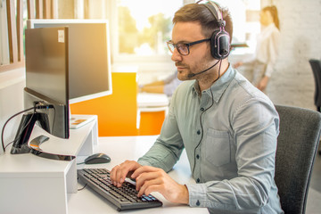 Wall Mural - Male professional call center telesales agent wearing headset using computer in customer care support service office.