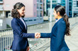 © Mangostar - Content businesswomen shaking hands. Side view of cheerful female colleagues in formal wear standing on street and greeting each other. Partnership concept