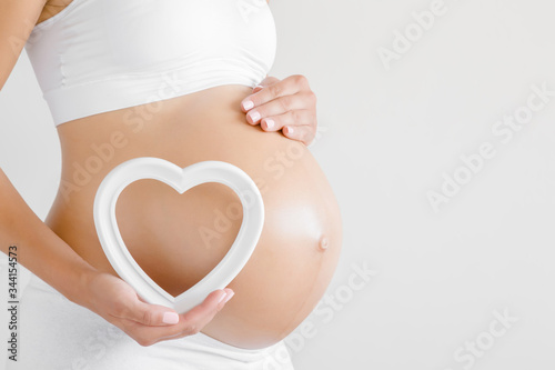 Fotografía Woman hand holding white empty frame of heart shape on naked belly