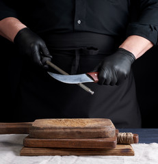 Wall Mural - chef in a black shirt and black latex gloves sharpen a kitchen knife on an iron sharpener with a handle