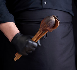 Wall Mural - chef in black latex gloves and a black uniform holds wooden vintage spoons