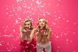 © LIGHTFIELD STUDIOS - Smiling blonde girls blowing air kiss at camera under falling confetti on pink background
