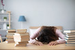 © BestForYou - Woman lying on table with books at home.