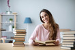 © BestForYou - Cheerful young woman sits at a table with books and does homework.