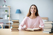 © BestForYou - Cheerful young woman sits at a table with books and does homework.