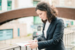 © Mangostar - Focused businesswoman reading papers on street. Concentrated middle aged businesswoman in formal wear holding folder with documents on street. Paperwork concept