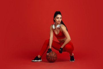 Beautiful young female athlete practicing in studio, monochrome red portrait. Sportive fit brunette model with ball and headphones. Body building, healthy lifestyle, beauty and action concept.