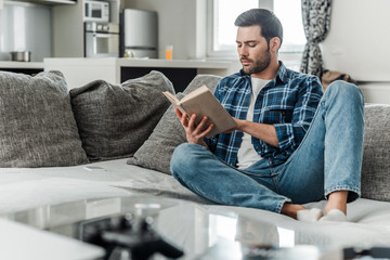 Selective focus of handsome man reading book on couch at home