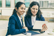 © Mangostar - Happy businesswomen with tablet pc in outdoor cafe. Cheerful female colleagues sitting at table, drinking coffee and using digital tablet in outdoor cafe. Wireless technology concept