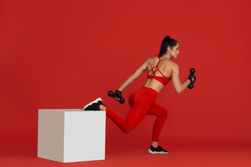 Motion. Beautiful young female athlete practicing in studio, monochrome red portrait. Sportive fit brunette model with jump box and weights. Body building, healthy lifestyle, beauty and action concept